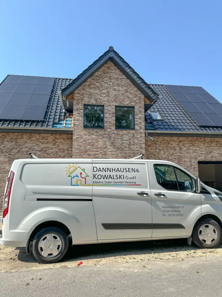 Ein Firmenfahrzeug von Dannhausen & Kowalski GmbH steht vor einem modernen Haus mit Solarpanelen auf dem Dach.