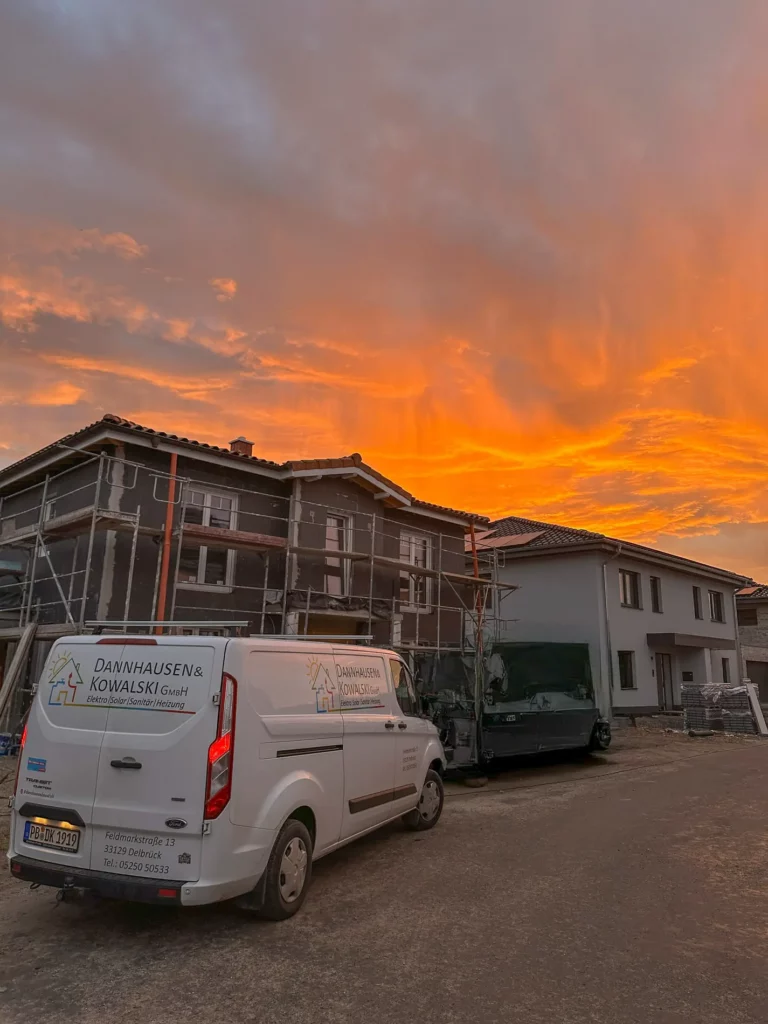 Bauarbeiten an zwei modernen Wohnhäusern bei Sonnenuntergang mit einem Firmenwagen im Vordergrund.