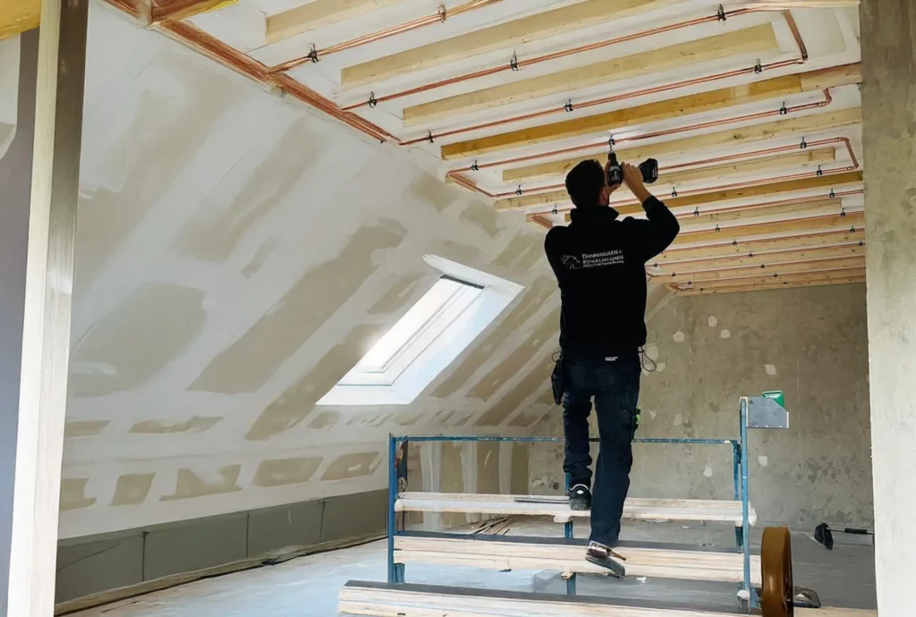 Ein Handwerker steht auf einer Leiter und installiert Deckenbeleuchtung in einem neu renovierten Dachraum.