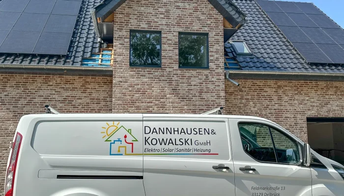 Ein weißer Transporter der Firma Dannhausen & Kowalski steht vor einem modernen Haus mit Solarpanelen auf dem Dach.