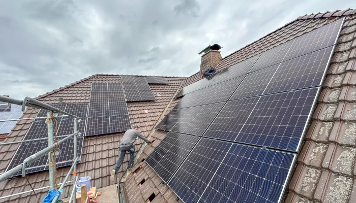 Ein Handwerker installiert Solarpanels auf einem Dach unter einem bewölkten Himmel.